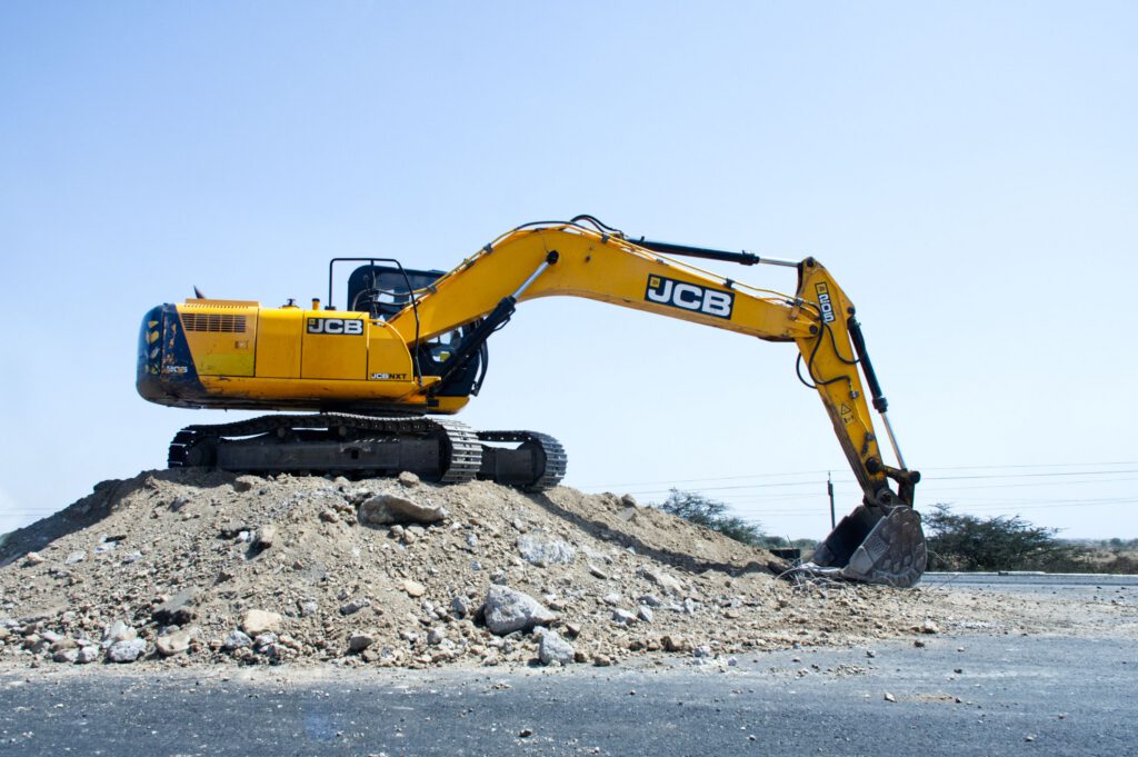 Home Yellow excavator on a pile of dirt at a construction site under clear blue sky.